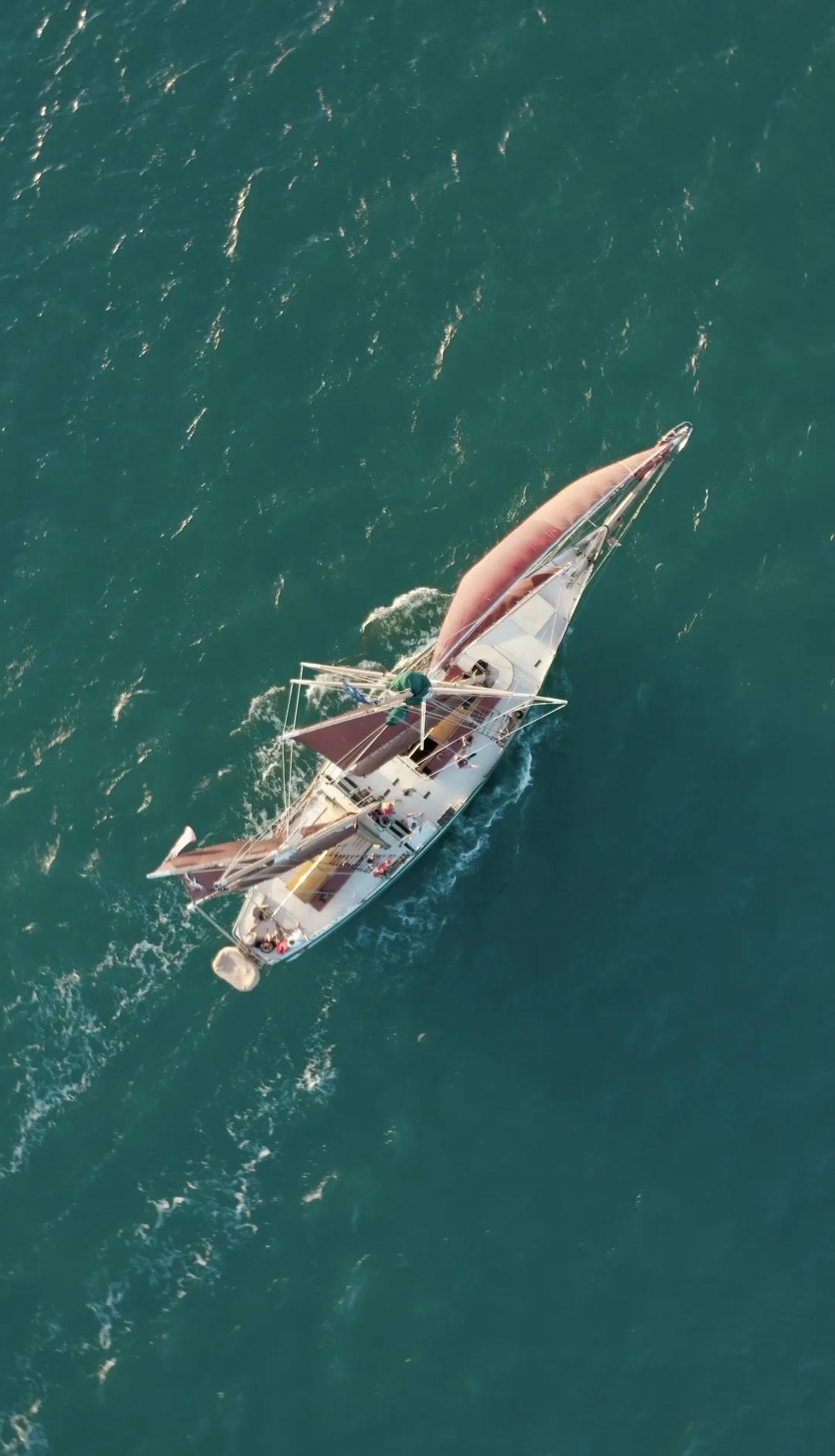 Dronebeeld van de Jolly Rover op zee · roodbruine zeilen tegen turkoois water