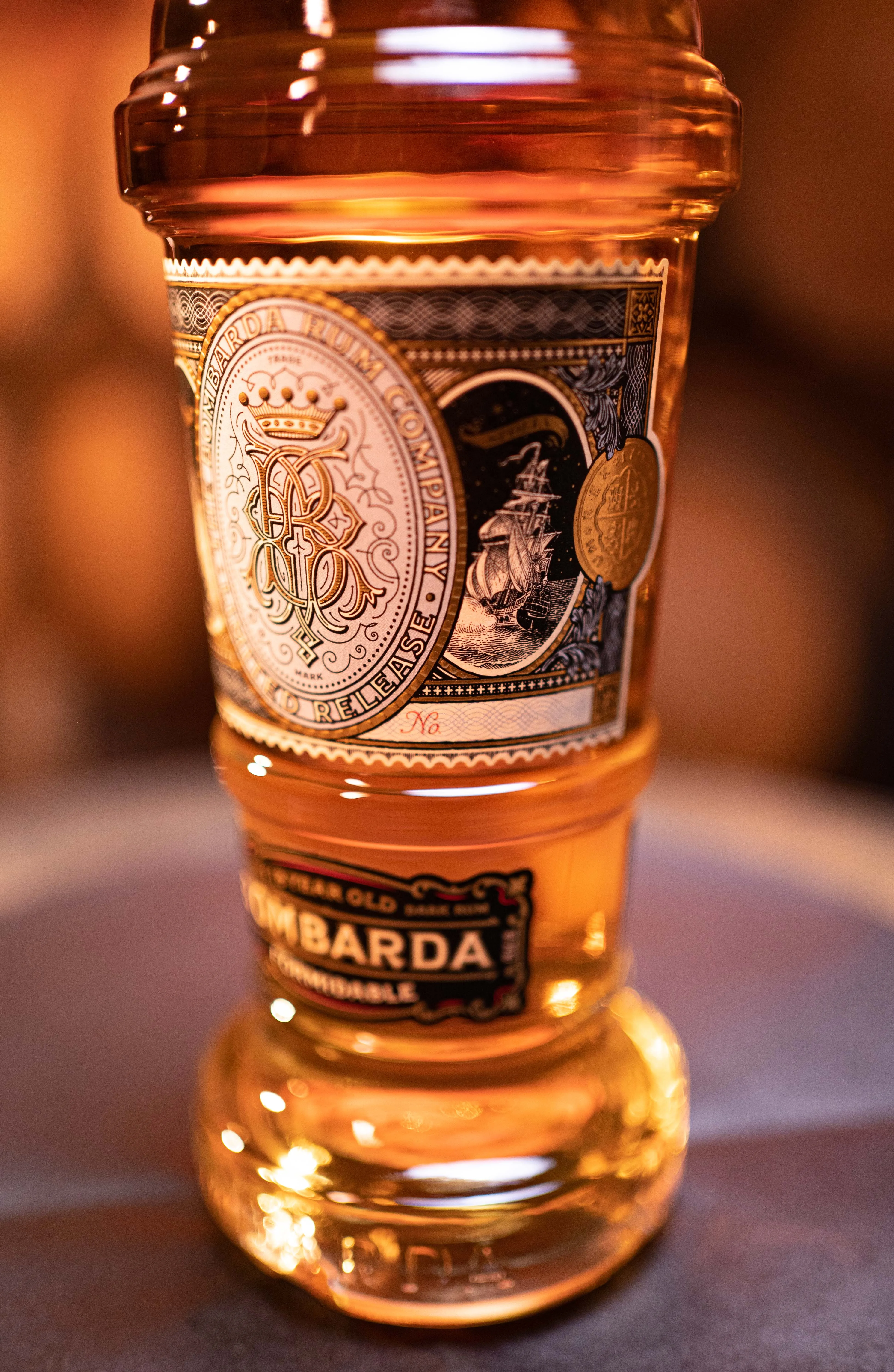 Detail-shot van het Bombarda label · vergulde monogram en silhouet van een schip