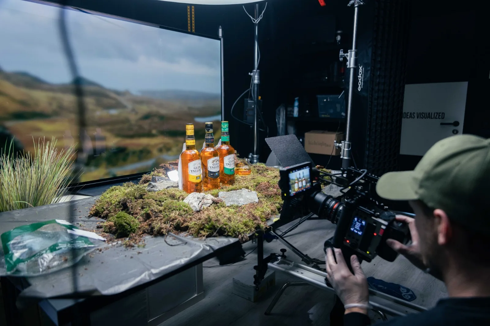 De volledige studio-setup: OLED TV als Schots landschap, mos-diorama op tafel, drie flessen, cinema-camera en lichtopstelling