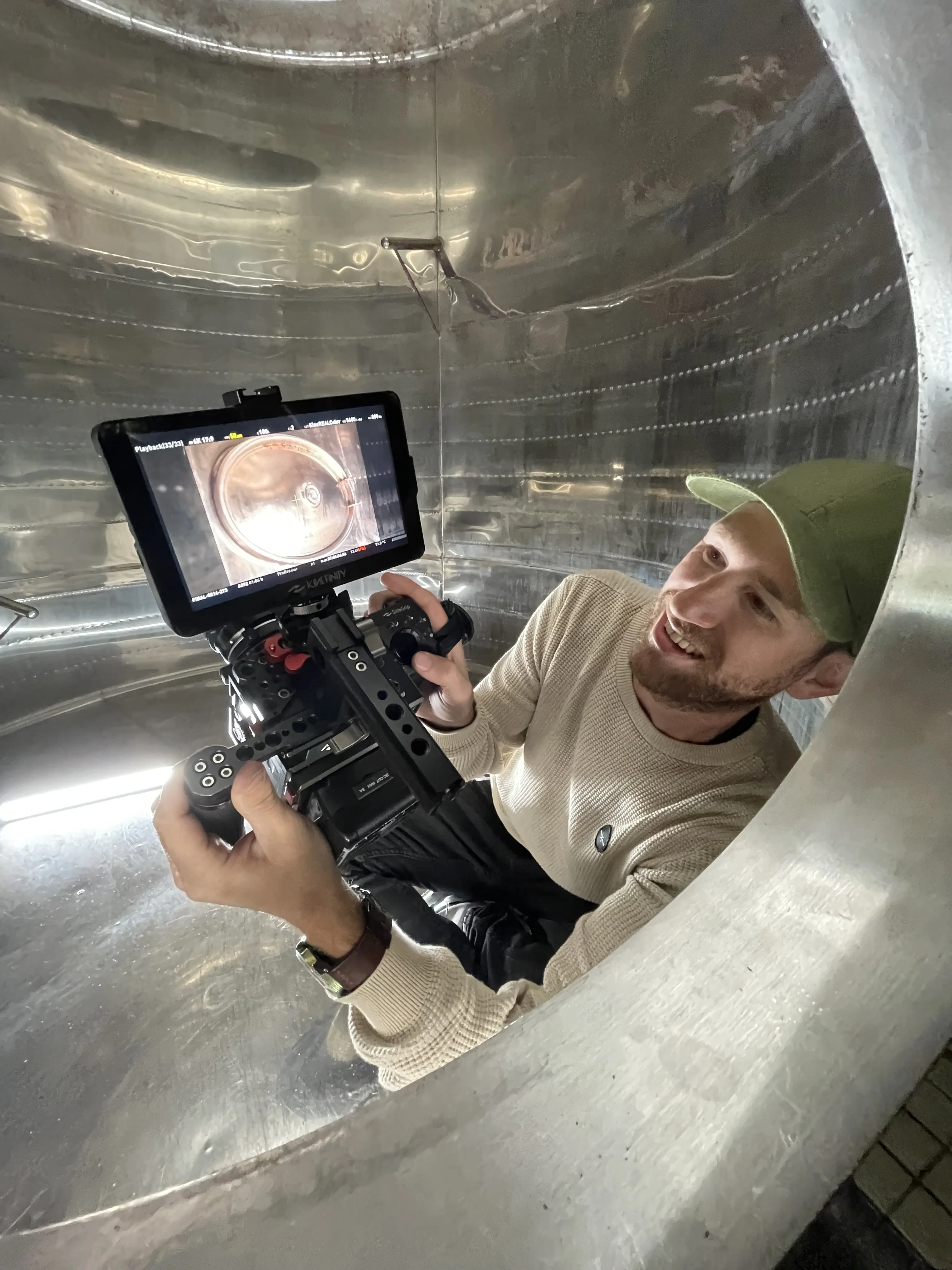 In de wijntank · Jeroen lacht met camera in de hand vanuit een lege roestvrijstalen tank